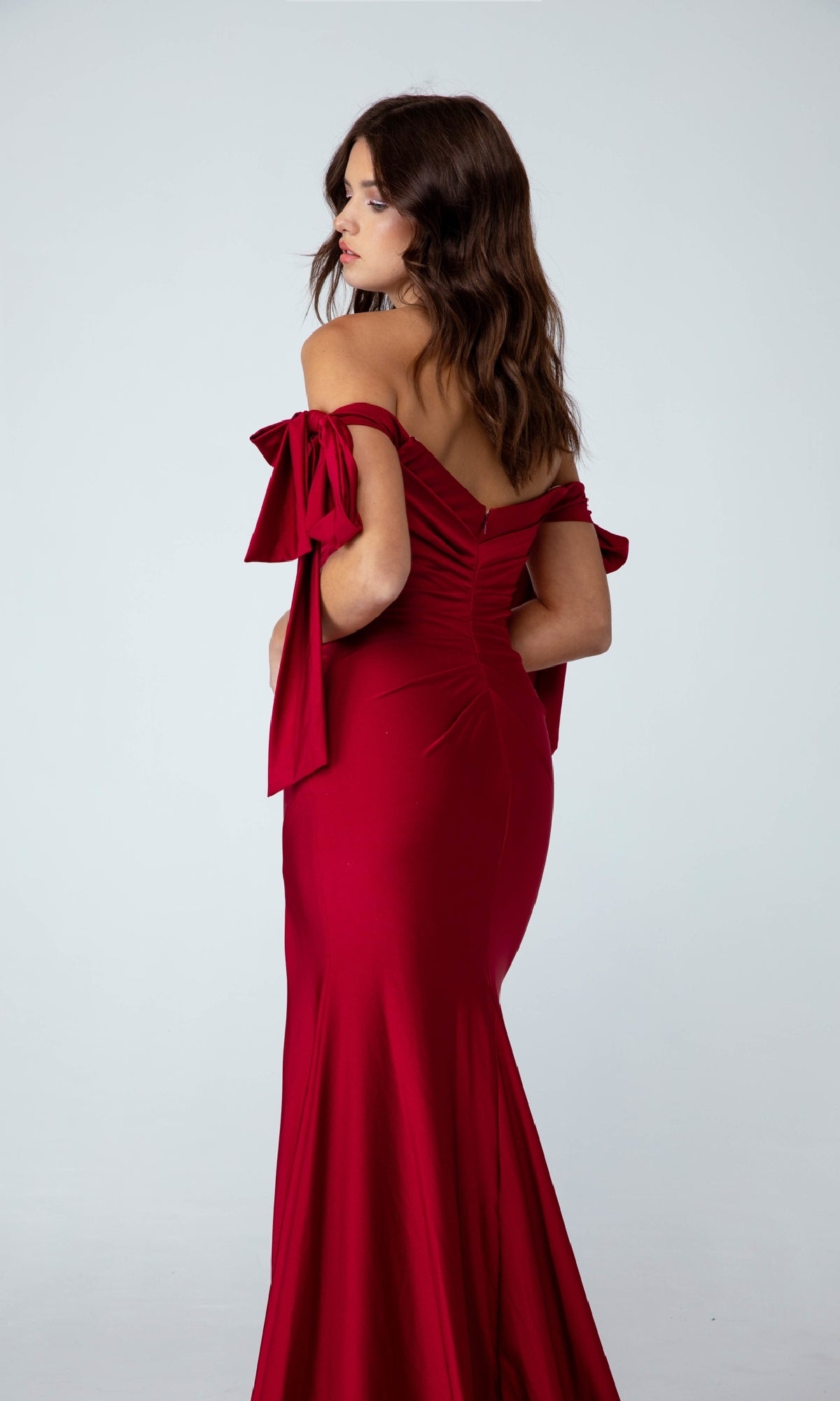 Woman in a Shoulder-Ties Long Jersey Prom Dress (Eureka 9181) poses with her back to the camera, highlighting the elegant silhouette of this affordable evening gown against a plain light background.